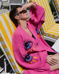 Person sitting on a sun chair wearing a pink kimono with evil eyes painted on it.