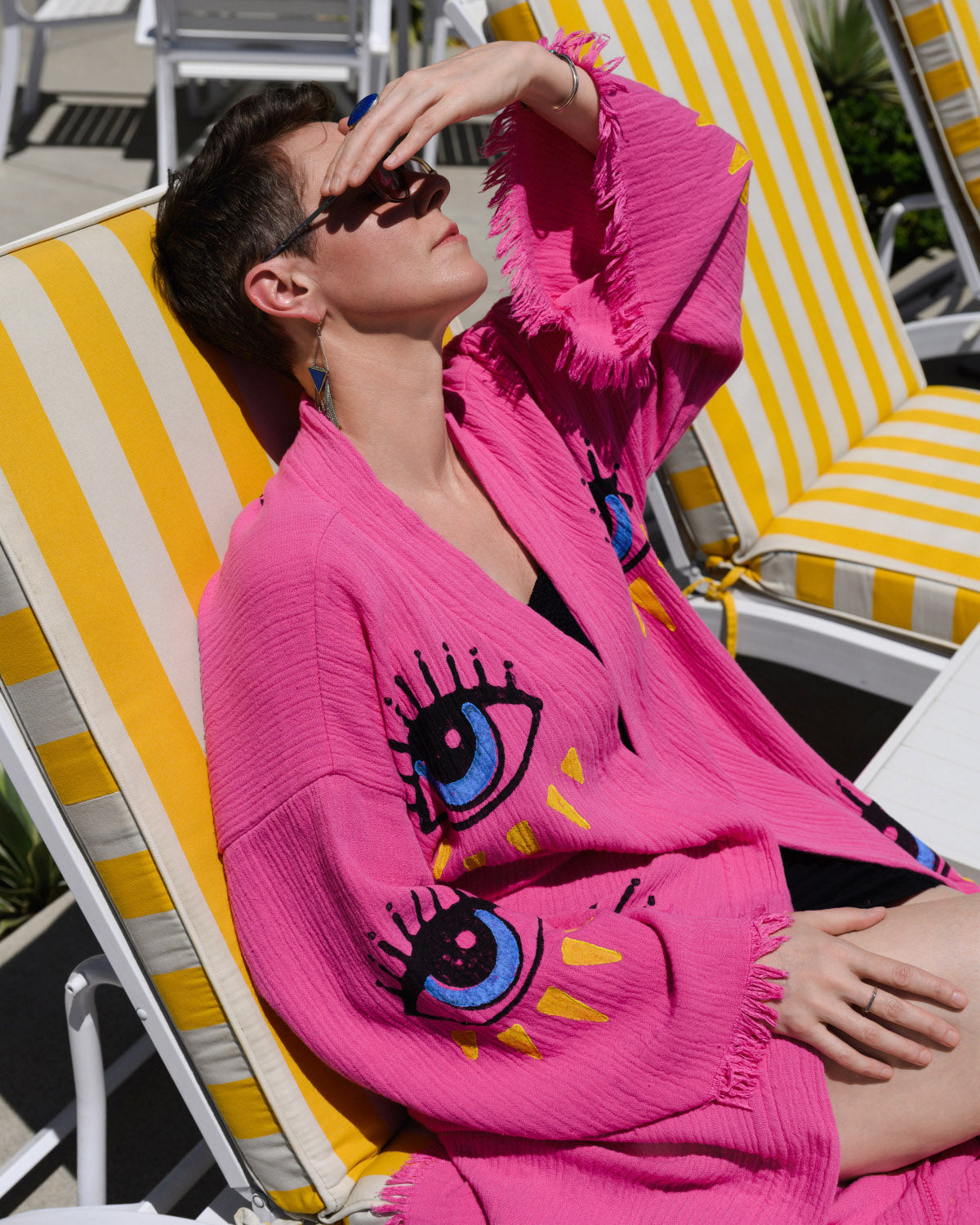 Person sitting on a sun chair wearing a pink kimono with evil eyes painted on it.